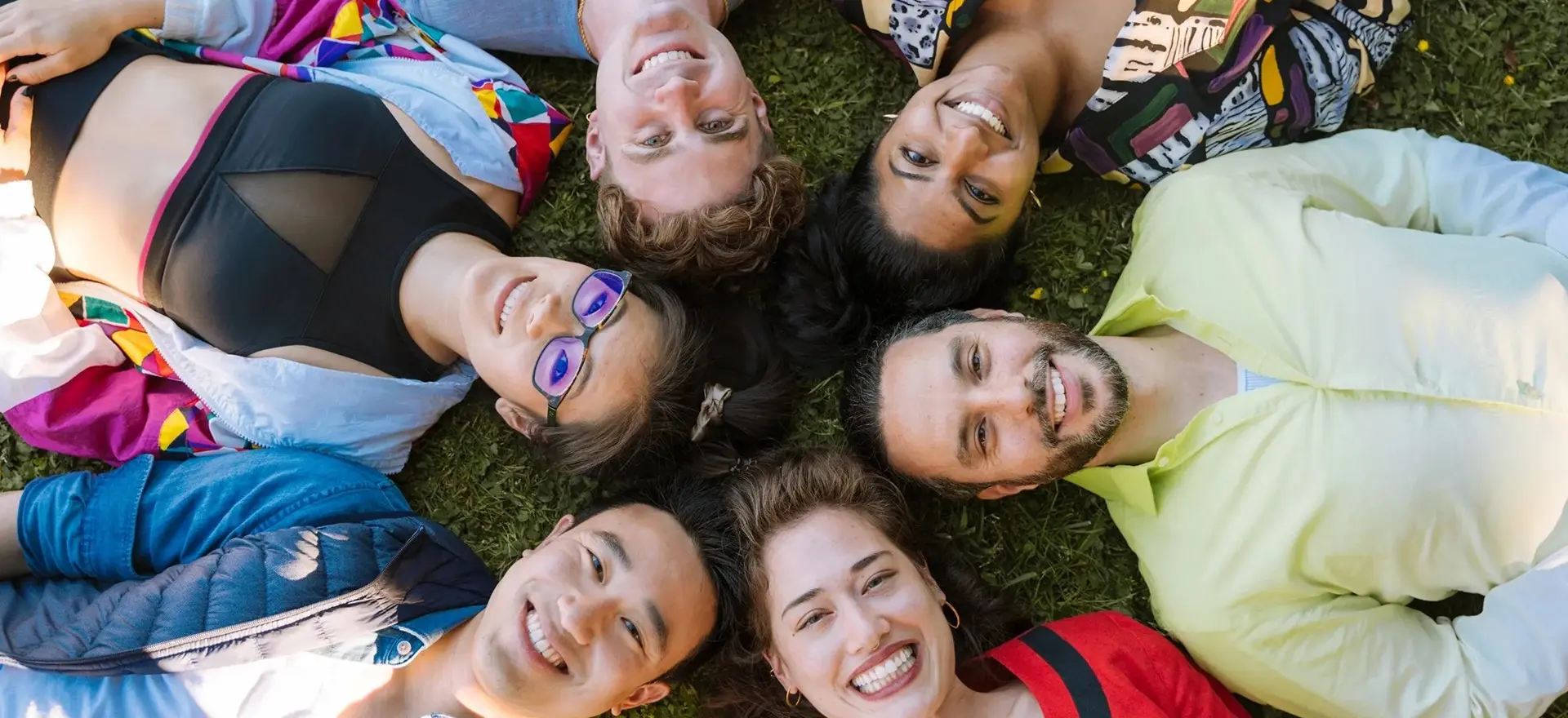 A group of people laying in the grass with their heads together.