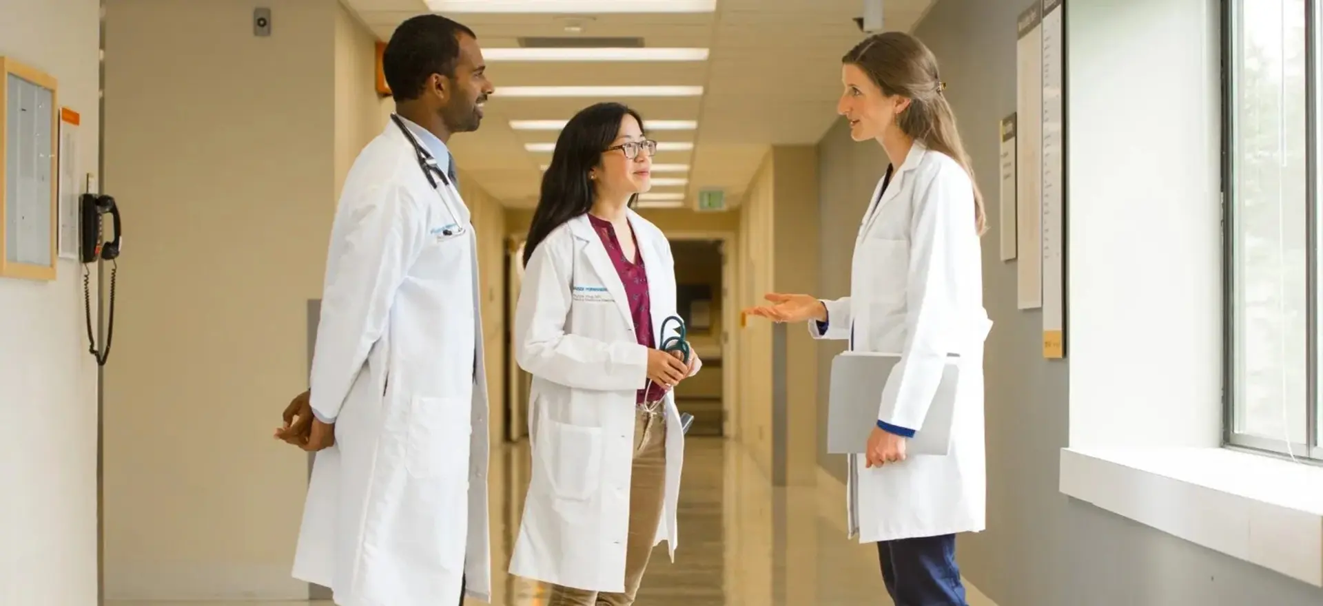 Three doctors are talking in a hospital hallway.