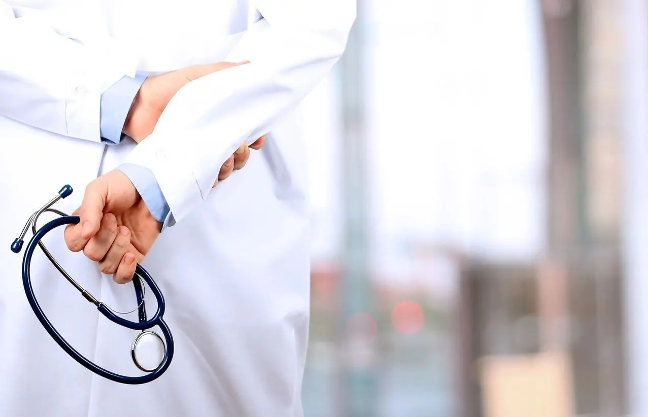 A person in white lab coat holding a pair of stethoscopes.