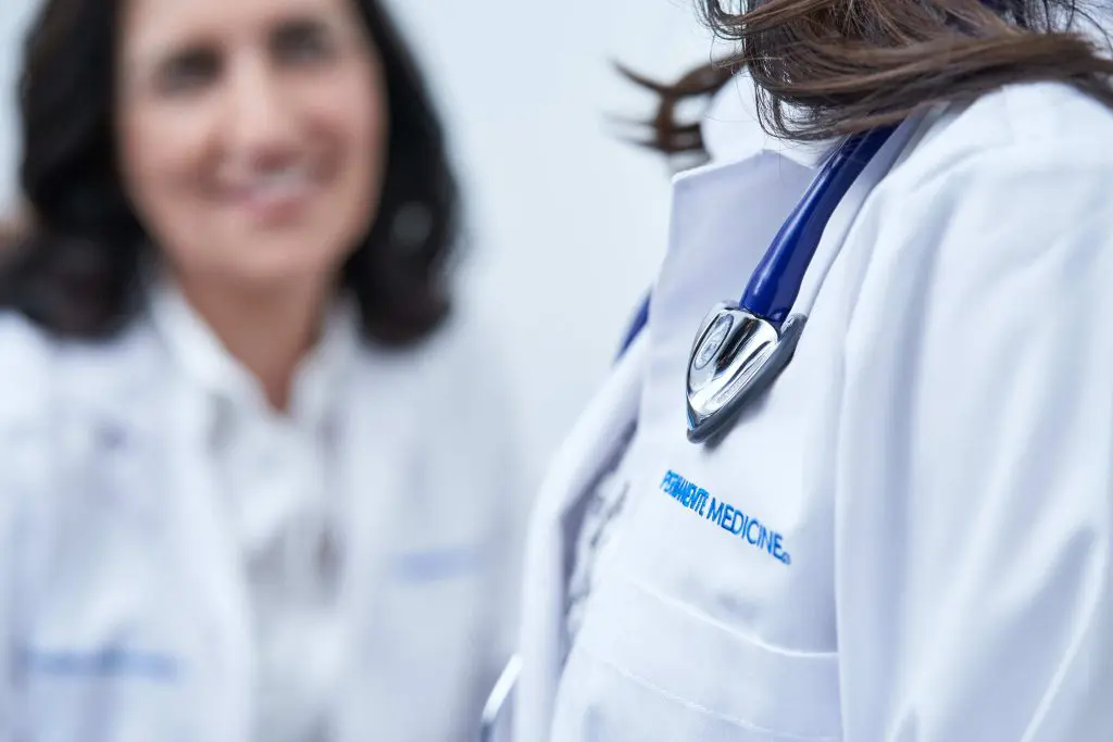 A woman standing next to another person wearing white lab coats.