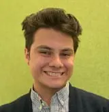 Portrait of a smiling young man with styled hair, wearing a checkered shirt and navy blazer against a lime green background.