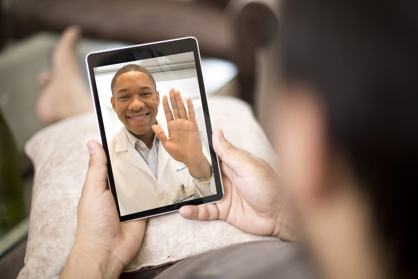 A person is holding up a tablet to take a picture of another person waving.