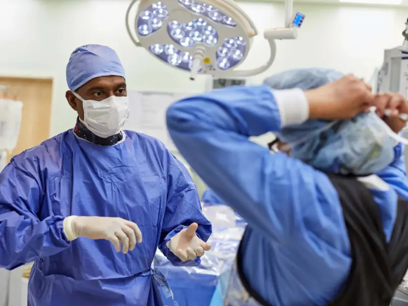 Two surgeons in blue gowns and masks are performing surgery.