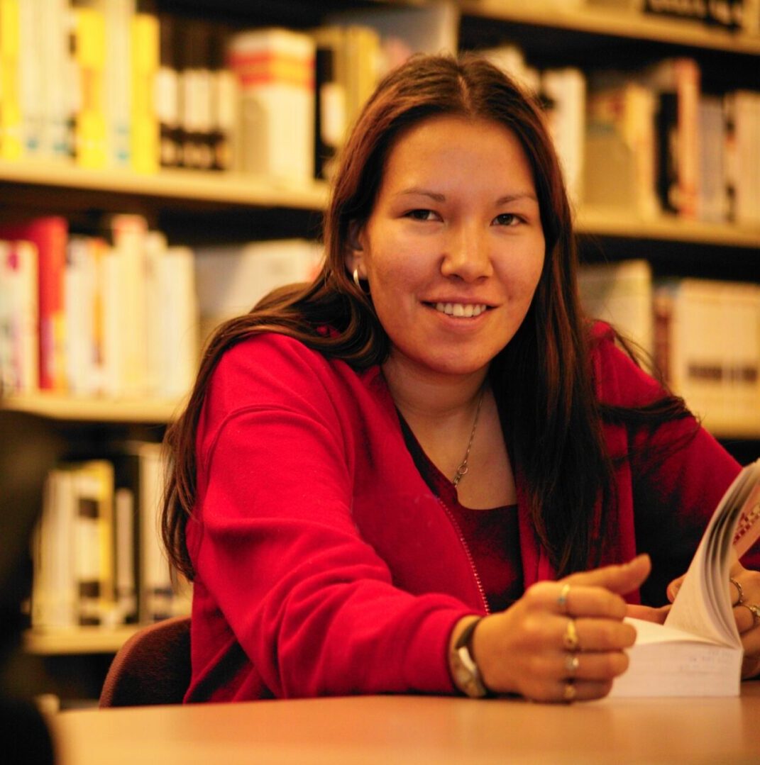 A woman sitting at a table in front of books.